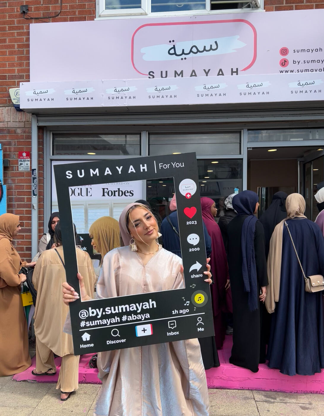 Girl holding SUMAYAH sign outside the storefront